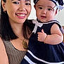 woman, baby, smile, portrait, navy_outfit, hat, bracelet, necklace, indoor, person, family, happy, holding, child, face, clothing, accessory, cute, skin, headwear