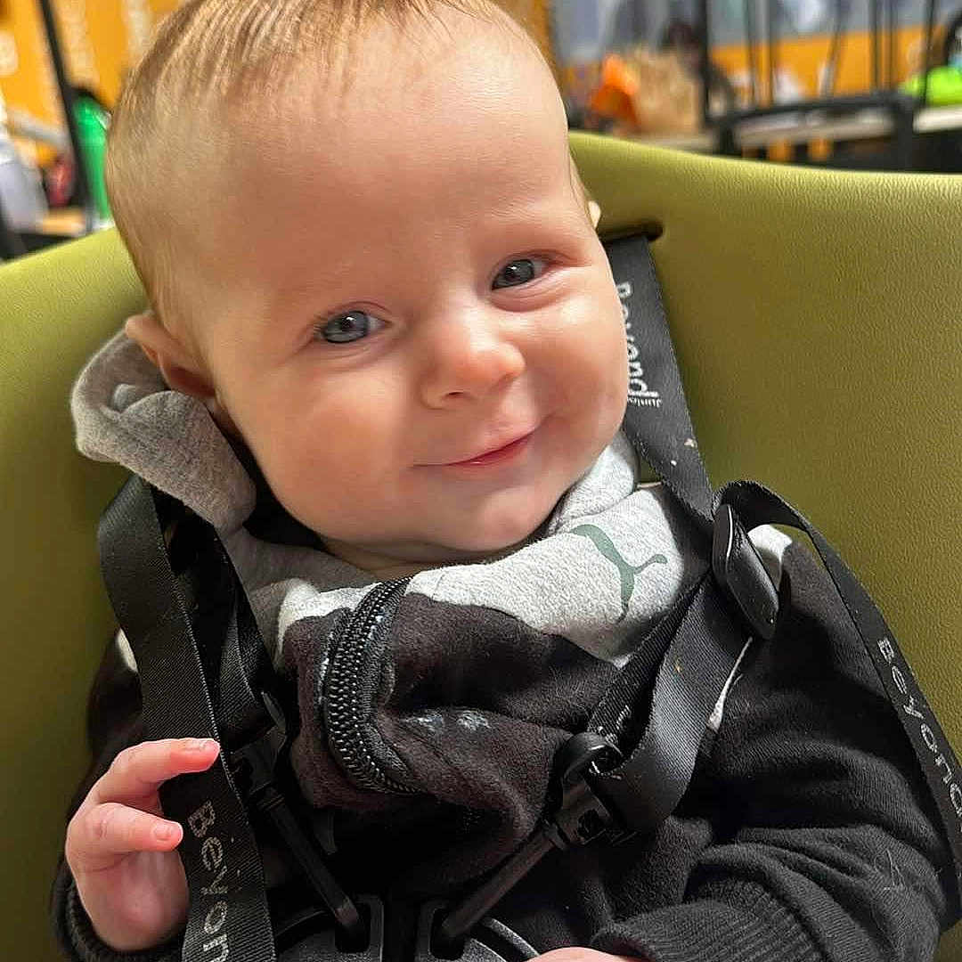 Wyatt is registered to the contest to win money with this photo: accessories, baby, babylaughing, blonde, bodypart, clothing, coat, face, finger, hair, hand, happy, head, jacket, person, photography, portrait, sitting, smile, strap