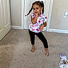 Lilyana is registered to the contest to win money with this photo: child, girl, portrait, smiling, posing, standing, floral_shirt, braids, hair_bows, indoors, bedroom, carpet, doors, wall, home, barefoot, fashion, playful, clothing, laundry