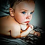 baby, child, blue_eyes, skin, face, hand, blanket, lying_down, portrait, expression, soft_lighting, indoor, close_up, cute, infant, curly_hair, fingertips, resting, young, thoughtful