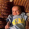 baby, blue, brown, child, clothing, cozy, cushion, cute, face, happy, indoor, infant, person, portrait, relaxing, smile, text, texture, tshirt, young