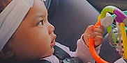 Mileena is registered to the contest to win money with this photo: baby, child, car_seat, headband, toy, colorful, hand, seat_belt, window, side_view, indoors, infant, clothing, face, person, car_interior, play, curious, young_child, closeup