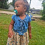 basketball_hoop, blue_bow, casual, child, curious, daytime, dress, floral_pattern, grass, greenery, nature, outdoor, pacifier, person, sandals, side_profile, suburban, summer_clothing, toddler, young_child