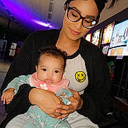 Mileena joined the competition — help win amazing prizes! woman, baby, glasses, headband, hair_buns, smile, holding, arcade, colorful_lights, indoor, casual_clothing, baby_pajamas, floral_pattern, seated, portrait, happy, person, technology, neon_lights, family