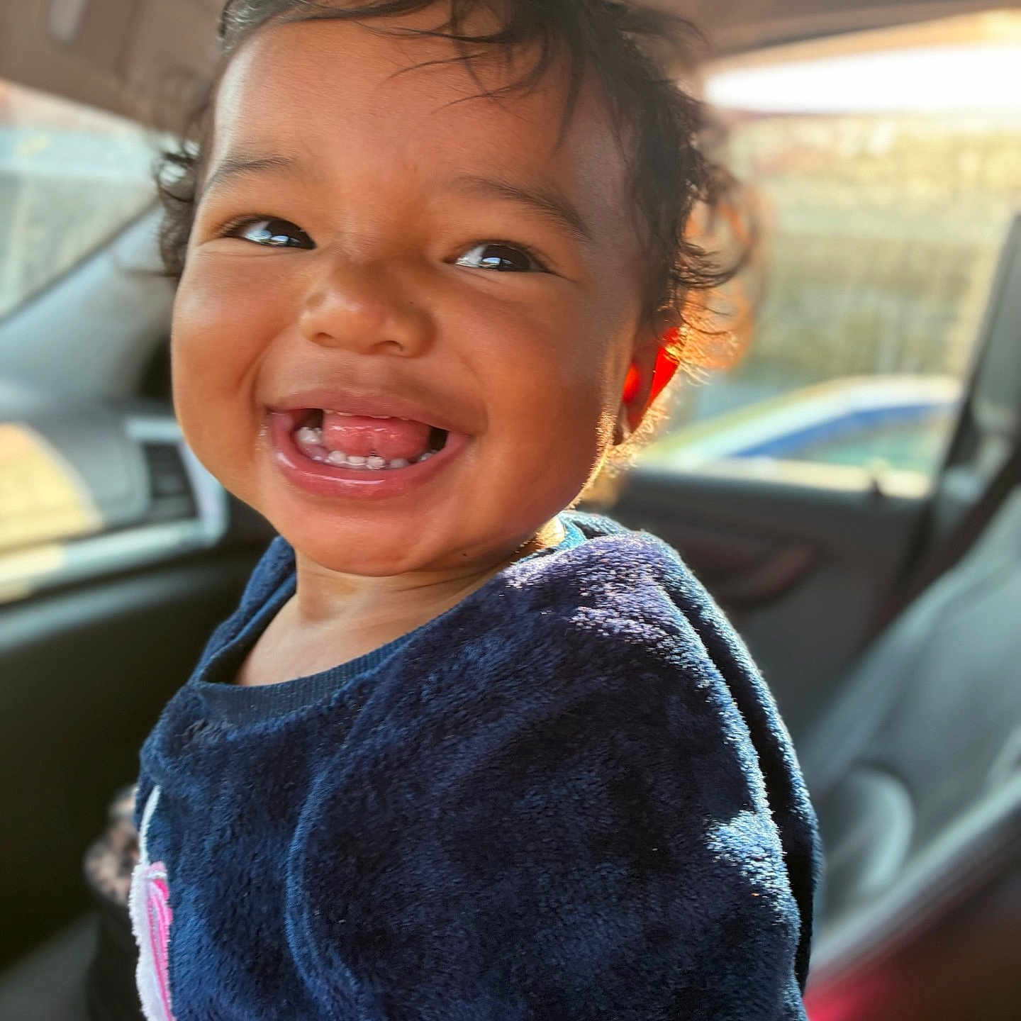 Mileena joined the competition — help win amazing prizes! baby, blue_sweater, car_interior, child, clothing, curly_hair, cute, face, happy, indoors, joyful, person, portrait, seat, smile, sunlight, teeth, toddler, window, young_child