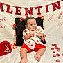 baby, infant, child, smile, valentine_banner, hearts, heart_decor, rose, kiss_marks, fairy_lights, red_shorts, heart_shirt, sitting, pillow, vase, chocolates, decorations, white_backdrop, photography, cute
