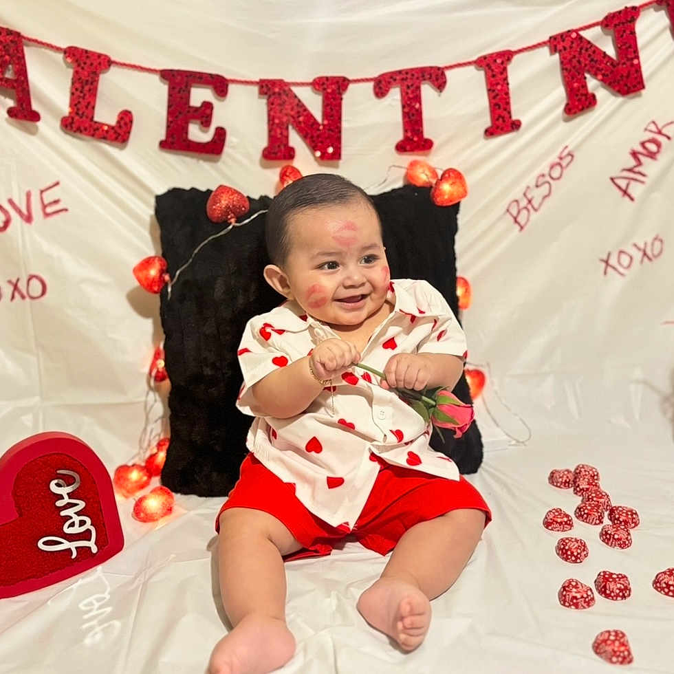 Leandro C is registered to the contest to win money with this photo: baby, child, chocolates, cute, decorations, fairy_lights, heart_decor, heart_shirt, hearts, infant, kiss_marks, photography, pillow, red_shorts, rose, sitting, smile, valentine_banner, vase, white_backdrop