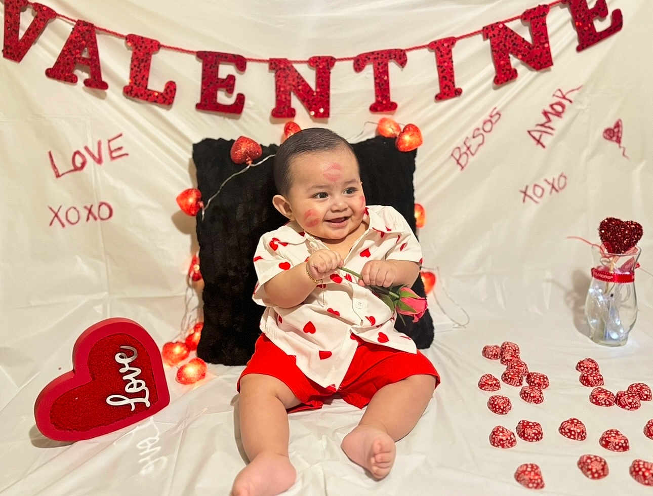 Leandro C is registered to the contest to win money with this photo: baby, infant, child, smile, valentine_banner, hearts, heart_decor, rose, kiss_marks, fairy_lights, red_shorts, heart_shirt, sitting, pillow, vase, chocolates, decorations, white_backdrop, photography, cute