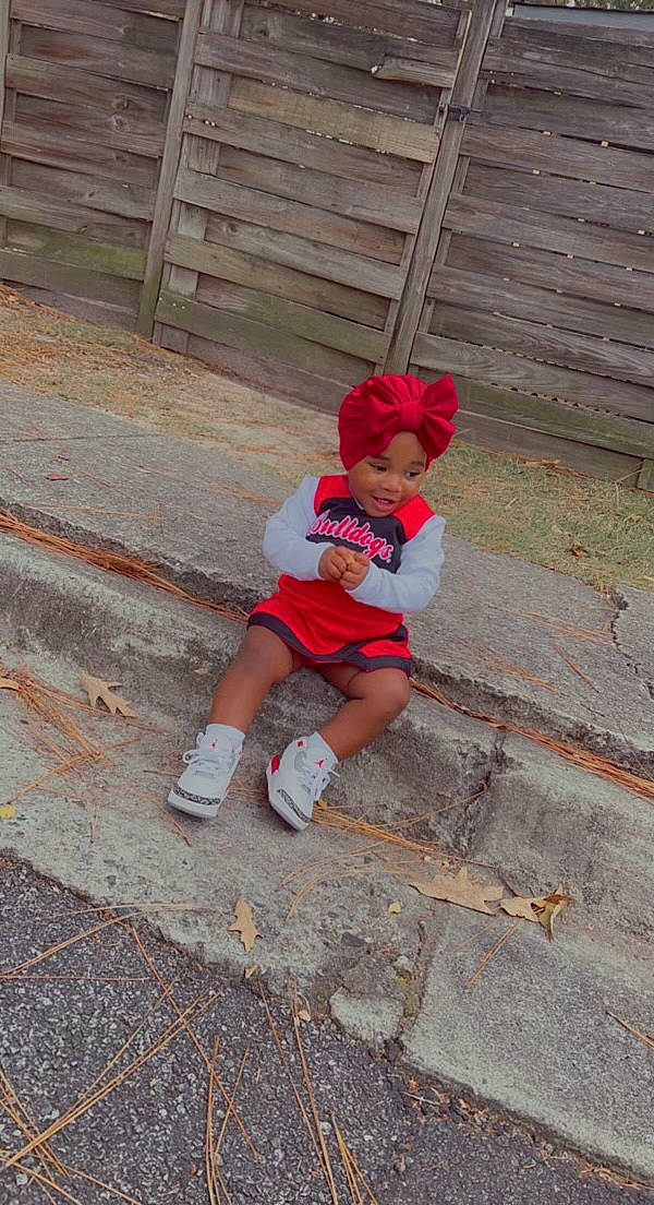 Madilyn joined the competition — help win amazing prizes! asphalt, child, fence, foot, fun, grass, hat, headwear, human_leg, leisure, magenta, person, plant, recreation, road_surface, sandal, shorts, sidewalk, sock, thigh