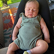 Grayson is registered to the contest to win money with this photo: baby, sleeping, romper, green_clothing, infant, person, legs, arms, outdoor, grass, plant, potted_plant, rug, floral_pattern, sock, seated, relaxed, daylight, home, comfort