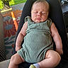baby, sleeping, romper, green_clothing, infant, person, legs, arms, outdoor, grass, plant, potted_plant, rug, floral_pattern, sock, seated, relaxed, daylight, home, comfort