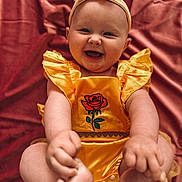 Winnie joined the competition — help win amazing prizes! baby, infant, smiling, yellow_outfit, headband, rose_embroidery, happy, cute, child, portrait, sitting, feet, hand, pink_background, fabric, soft_texture, chubby, playful, indoors, closeup