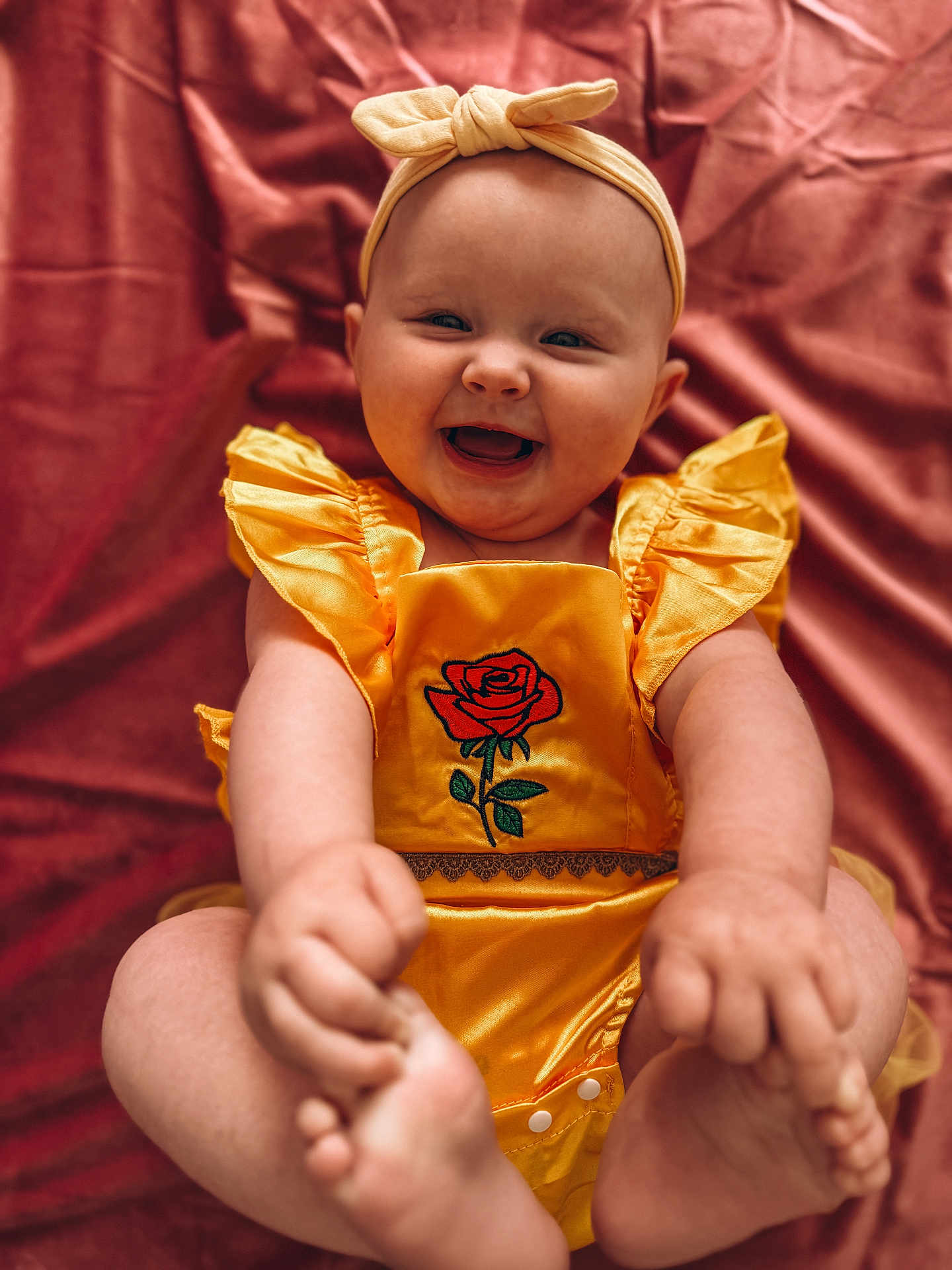 Winnie joined the competition — help win amazing prizes! baby, infant, smiling, yellow_outfit, headband, rose_embroidery, happy, cute, child, portrait, sitting, feet, hand, pink_background, fabric, soft_texture, chubby, playful, indoors, closeup
