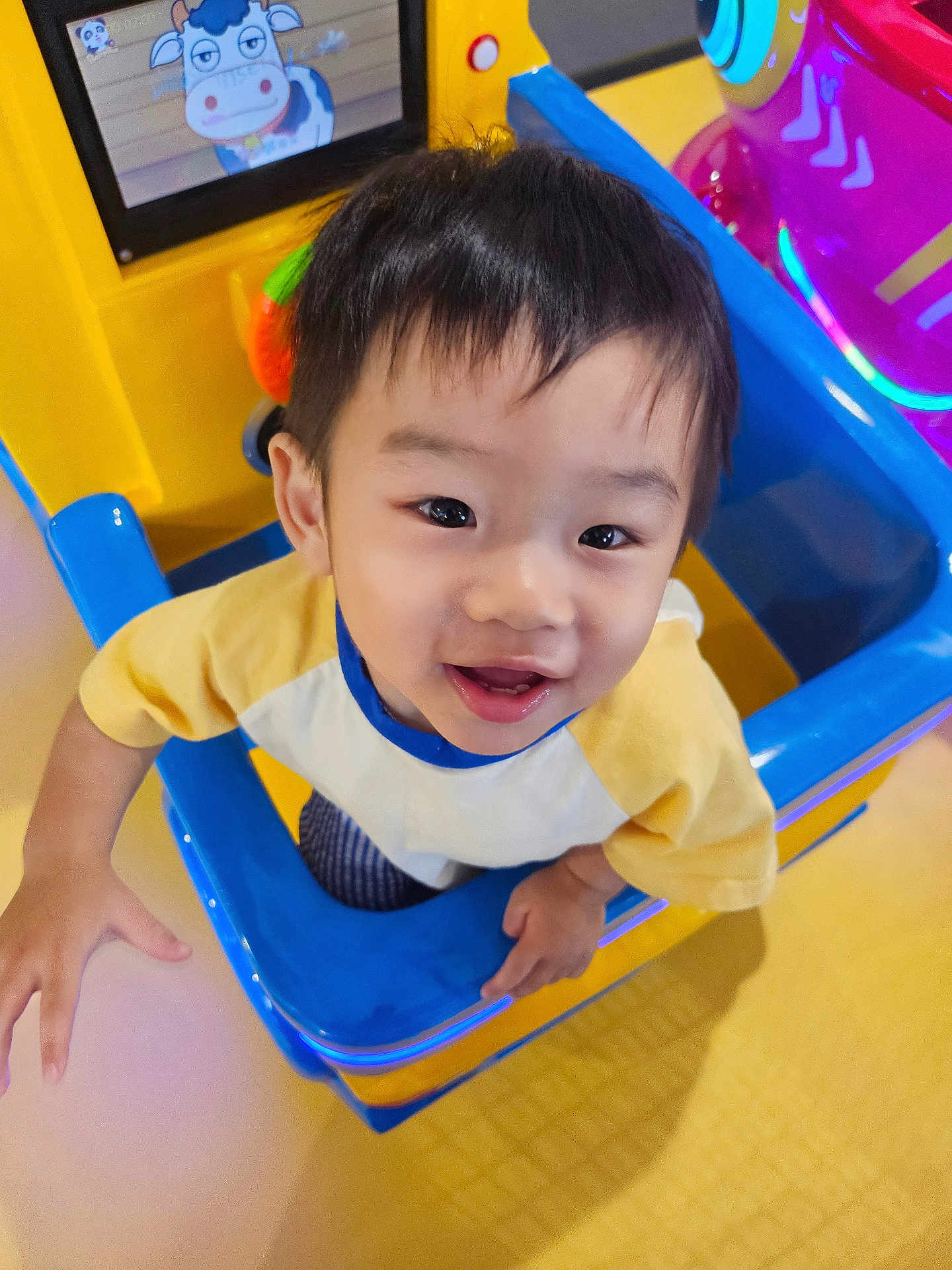 Sean joined the competition — help win amazing prizes! child, toddler, smiling, playground, play_structure, colorful, indoor, happy, face, person, toy, screen, cartoon, yellow, blue, clothing, short_hair, cute, joyful, playroom