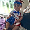 adult, baby, bed, blanket, blue, child, clothing, curious, hand, hat, indoor, infant, person, portrait, red, sitting, stars, stripes, white, window