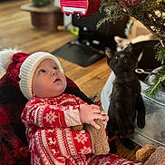 Logan joined the competition — help win amazing prizes! baby, child, kitten, cat, christmas_tree, ornament, holiday, pajamas, hat, red, white, floor, wooden_floor, indoor, decor, cute, curious, pet, cozy, winter