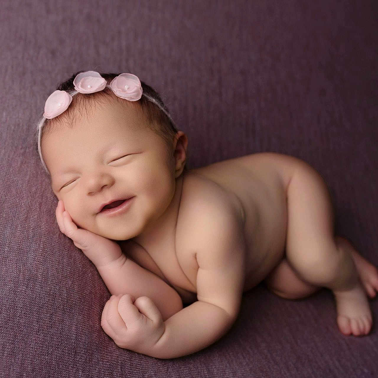 Esmée a rejoint le concours — aidez-le/la à gagner de superbes lots ! baby, newborn, sleeping, smiling, headband, flower, purple_blanket, skin, infant, cute, peaceful, lying_down, hand_near_face, portrait, soft_texture, closed_eyes, adorable, child, resting, small