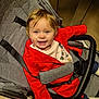 baby, blue_eyes, child, clothing, cute, elevator, floor, gray_fabric, happy, harness, indoor, person, portrait, red_jacket, seat, smile, sneakers, stroller, toddler, young_child