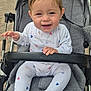 baby, child, smiling, stroller, onesie, heart_pattern, outdoor, playground, park, happy, infant, person, seat, toy, hand, footwear, fabric, headwear, face, daylight
