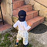 Liam a rejoint le concours — aidez-le/la à gagner de superbes lots ! back_view, bunny_print, cap, casual_clothing, child, concrete, daylight, grass, hat, outdoor, pants, person, shoes, stairs, steps, tiles, toddler, walking, wall, young_child