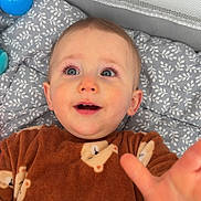 Liam a rejoint le concours — aidez-le/la à gagner de superbes lots ! baby, child, onesie, bear_pattern, blanket, toy, blue_ball, orange_ball, smiling, reaching_hand, indoor, cute, happy, face, head, infant, playpen, soft_fabric, lying_down, curious