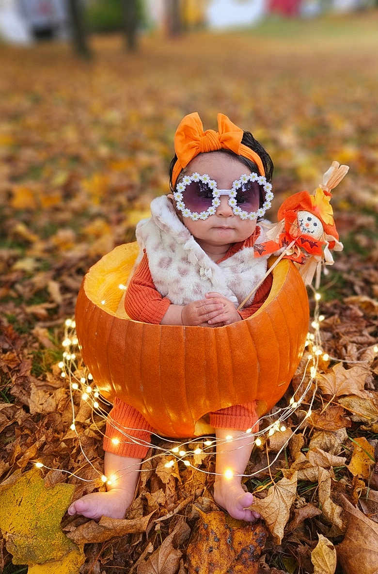 Selena joined the competition — help win amazing prizes! baby, pumpkin, autumn_leaves, fall, outdoor, child, sunglasses, headband, orange_clothing, scarecrow, decorative_lights, cute, seasonal, festive, nature, portrait, sitting, leaf_litter, baby_accessories, fall_fashion