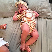 Ida-Belle is registered to the contest to win money with this photo: baby, infant, bed, pillow, headband, striped_clothing, lying_down, hand, foot, skin, person, child, indoors, cozy, cute, sleepwear, soft_texture, human, young, relaxing