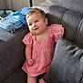 baby, infant, pink_dress, couch, gray_cushion, smile, indoor, child, cute, relaxed, furniture, footwearless, portrait, person, living_room, bag, cartoon, blue, seated, happy