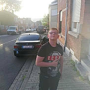 Jean Alexandre a rejoint le concours — aidez-le/la à gagner de superbes lots ! boy, child, glasses, black_tshirt, skull_graphic, sidewalk, brick_building, car, open_car_door, street, urban, daylight, casual, thumbs_up, young_person, residential_area, pavement, vehicle, outdoor, person