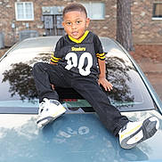 Mason joined the competition — help win amazing prizes! child, boy, portrait, outdoor, car, vehicle, football_jersey, steelers, sportswear, sneakers, black_clothing, yellow, brick_building, tree, driveway, sitting, smiling, short_hair, reflection, fashion