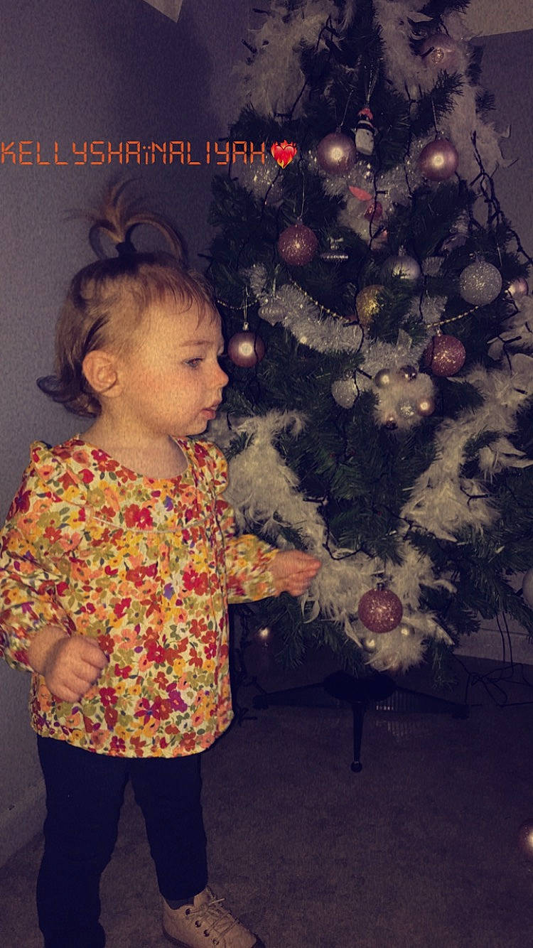 Shaïna participe au concours pour gagner de l'argent avec cette photo : baby_toddler_clothing, christmas_ornament, christmas_tree, evergreen, eye, fashion, hair, hairstyle, happy, holiday_ornament, human, human_body, organ, ornament, people, person, plant, standing, tints_and_shades, toddler