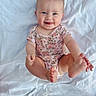 baby, child, infant, smiling, tongue_out, blue_eyes, floral_onesie, barefoot, hands, feet, white_blanket, cute, happy, sitting, portrait, playful, skin, person, indoors, closeup