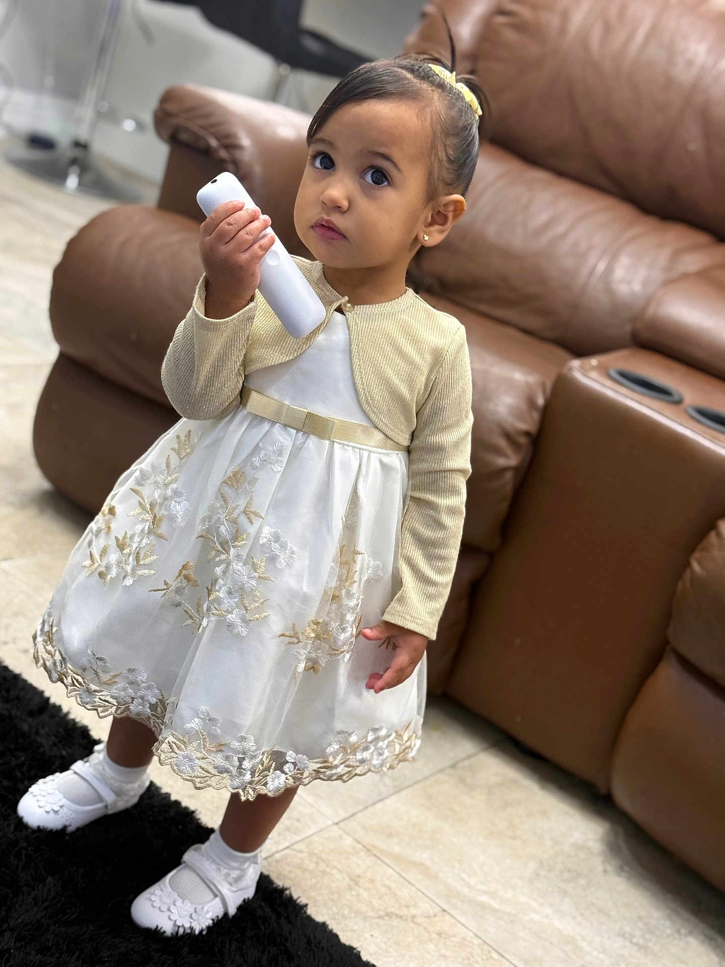 Brithanie is registered to the contest to win money with this photo: brown_sofa, carpet, child, curious, cute, dress, floor, girl, gold, indoor, living_room, person, portrait, remote_control, shoes, small, socks, standing, white, young