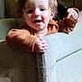 Atticus is registered to the contest to win money with this photo: toddler, child, baby, playpen, hands, pointing, brown_sweater, indoor, smiling, face, curly_hair, happy, cute, person, portrait, young_child, infant, furniture, cozy, light