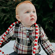 Cameron is registered to the contest to win money with this photo: baby, child, plaid_shirt, blue_eyes, red_hair, bead_garland, outdoor, pine_tree, blanket, sitting, curious, winter_clothing, casual, cute, portrait, holiday_decor, festive, infant, young_child, nature