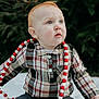 baby, child, plaid_shirt, blue_eyes, red_hair, bead_garland, outdoor, pine_tree, blanket, sitting, curious, winter_clothing, casual, cute, portrait, holiday_decor, festive, infant, young_child, nature