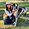 woman, dog, great_dane, grass, outdoor, smiling, hat, crouching, sunlight, barn, trees, casual_clothing, pet, animal, happy, friendship, daytime, nature, leisure, black_and_white