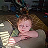 Waylon is registered to the contest to win money with this photo: child, toddler, sleepy, sunlight, indoor, living_room, carpet, toy, blanket, chair, furniture, person, face, hair, clothing, arm, legs, shadow, cozy, relaxing
