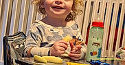 Waylon joined the competition — help win amazing prizes! toddler, child, smiling, curly_hair, snack, table, toy_car, baby_bottle, crib, chair, clothing, indoor, happy, face, person, playful, furniture, baby, cute, munching