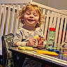 toddler, child, smiling, curly_hair, snack, table, toy_car, baby_bottle, crib, chair, clothing, indoor, happy, face, person, playful, furniture, baby, cute, munching
