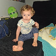 Waylon is registered to the contest to win money with this photo: toddler, child, couch, cookie, plush_toy, blanket, curly_hair, indoor, portrait, sitting, blue_clothing, striped_pants, wall_photos, carpet, foot, hand, expression, toy, room, person