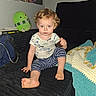 toddler, child, couch, cookie, plush_toy, blanket, curly_hair, indoor, portrait, sitting, blue_clothing, striped_pants, wall_photos, carpet, foot, hand, expression, toy, room, person