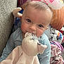 baby, infant, plush_toy, couch, pillow, blanket, blue_clothing, smiling, cute, indoors, child, soft_toy, face, person, cozy, closeup, happy, young_child, comfort, home
