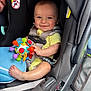 baby, car_seat, toy, smiling, child, infant, safety_harness, colorful, cute, indoors, seatbelt, car_interior, small_child, happy, person, closeup, foot, hand, yellow_clothing, playful