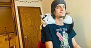 Kikaroo is registered to the contest to win money with this photo: beanie, black_and_white_cat, casual, cat, cozy, decor, furniture, home, indoor, man, plaid_pants, portrait, relaxed, seated, shoulder_cat, smile, string_lights, tshirt, wooden_door, young_adult