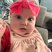 Ellie joined the competition — help win amazing prizes! baby, infant, headband, pink, dress, corduroy, closeup, face, indoor, couch, cushion, child, person, young, cute, wide_eyes, portrait, seated, soft_lighting, apparel