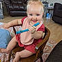 child, toddler, smiling, blue_eyes, pink_bib, red_dress, wooden_chair, toy, indoor, living_room, carpet, furniture, happy, cute, person, hair_tie, baby, flooring, lamp, table