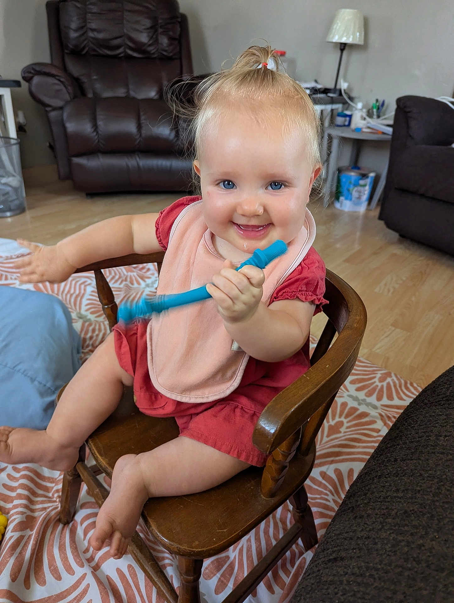 Emmilynn joined the competition — help win amazing prizes! child, toddler, smiling, blue_eyes, pink_bib, red_dress, wooden_chair, toy, indoor, living_room, carpet, furniture, happy, cute, person, hair_tie, baby, flooring, lamp, table
