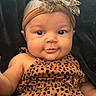 baby, infant, child, face, headband, bow, leopard_print, clothing, cute, smile, portrait, skin, eyes, cheeks, sitting, indoors, black_background, fashion, headwear, person