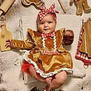 Julia is registered to the contest to win money with this photo: baby, blanket, christmas, costume, cute, decoration, dress, festive, flour, gingerbread, holiday, infant, plush_toy, red_bow, rolling_pin, smiling, soft_toy, table, wood_surface, wooden_cutting_board